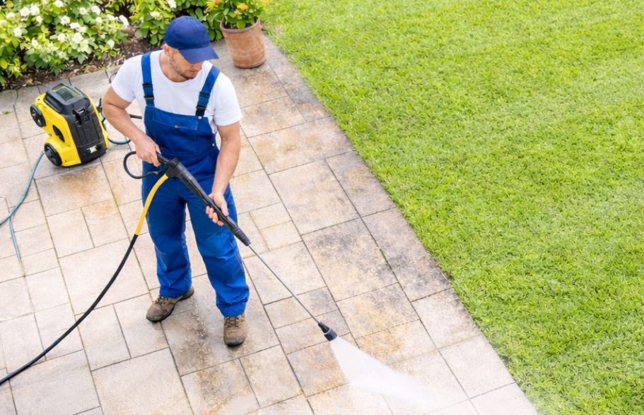 Terrassenreinigung Göttingen und Umgebung Mann reinigt mit Hochdruckreiniger eine Terrasse in einem Garten.