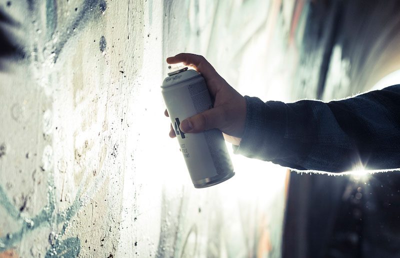 Graffiti-Entfernung in Göttingen und Umgebung Eine Hand sprüht Graffiti an eine Wand mit lebendigen Farben.